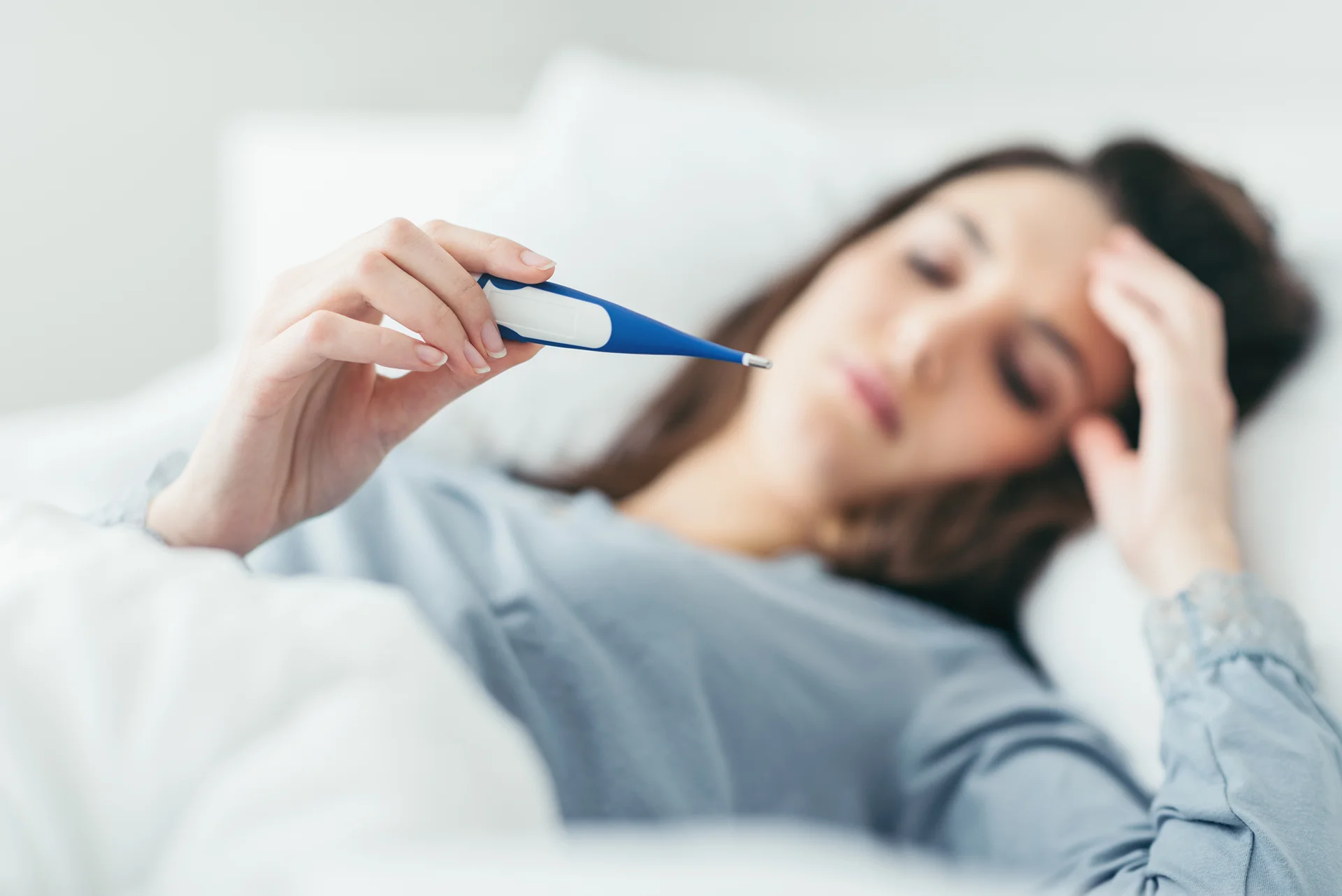 a sick woman stays in bed while checking her temperature