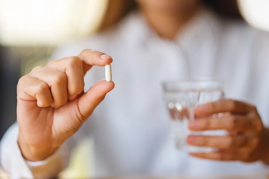 a woman holding a white pill and a glass of water
